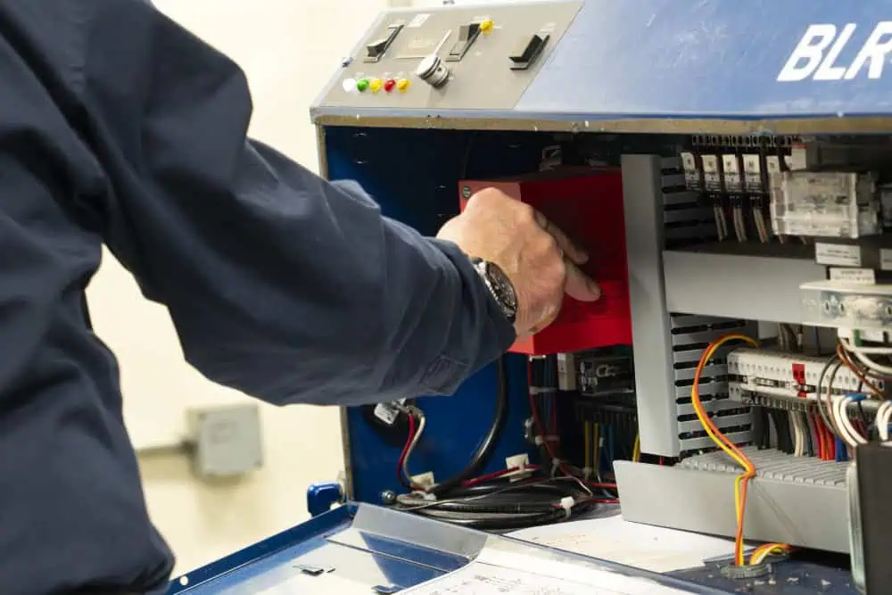 A factory worker, a man, is diligently working on a machine, surrounded by equipment and tools in an industrial environment Image