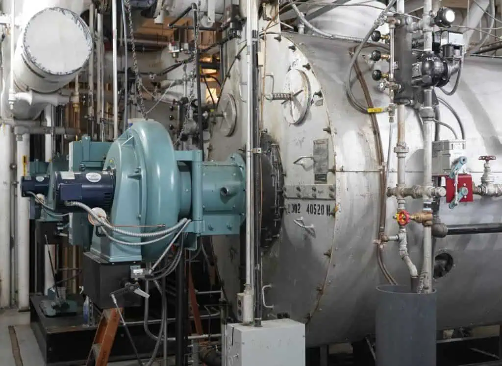 A large industrial boiler setup with piping and a motorized fan system.