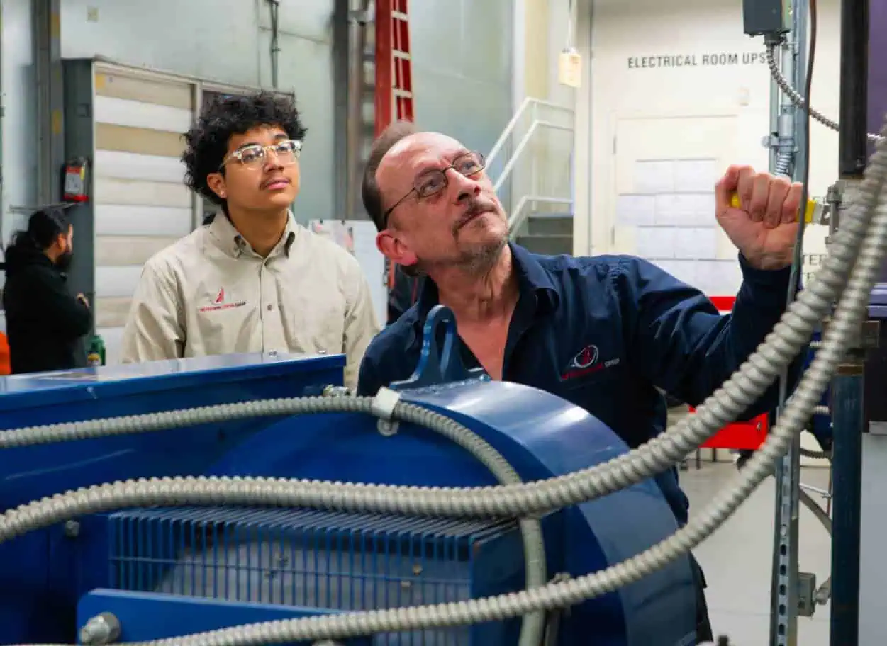 A-man-adjusts-equipment-while-another-man-observes-in-a-workshop-or-training-facility