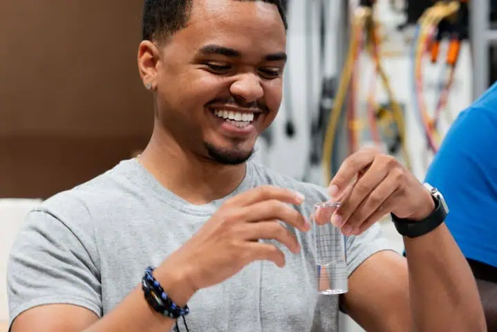 A man with a smile holds a glass of water, highlighting a one-day bootcamp on water quality tests and treatment optimization.