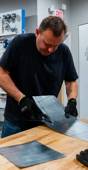 A person is cutting metal sheets on a wooden workbench while wearing gloves.