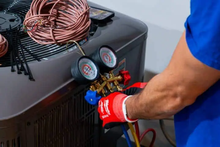 A technician wearing red gloves is using pressure gauges on an air conditioning unit