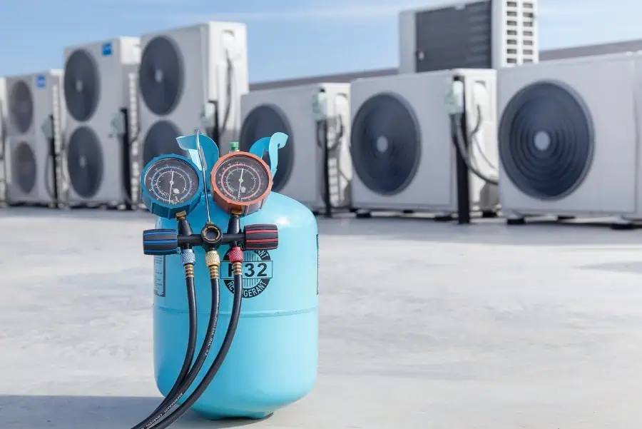 Blue refrigerant tank with pressure gauges on a rooftop with air conditioning units.