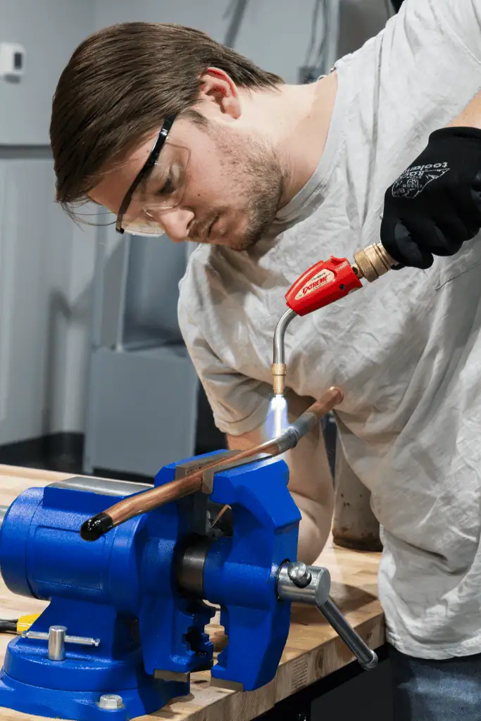 Person using a torch to heat a copper pipe secured in a vise