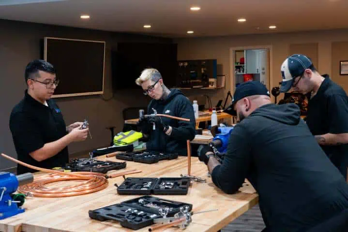 Four individuals working at a table in a workshop, using various tools and equipment.