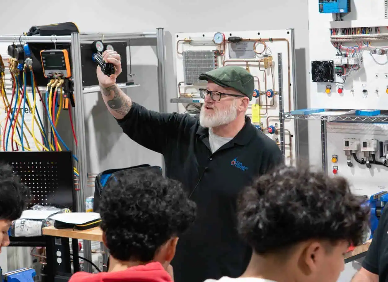 Instructor-gesturing-to-students-in-a-trades-classroom-with-equipment-in-the-background