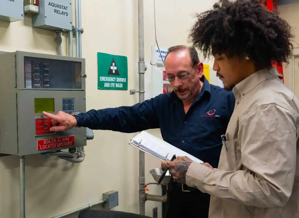 Man-pointing-at-a-control-panel-while-another-holds-a-clipboard
