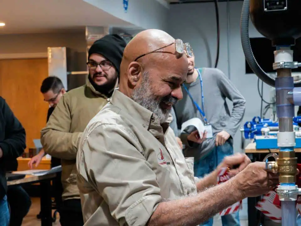 Man smiling while working on equipment in a workshop with others