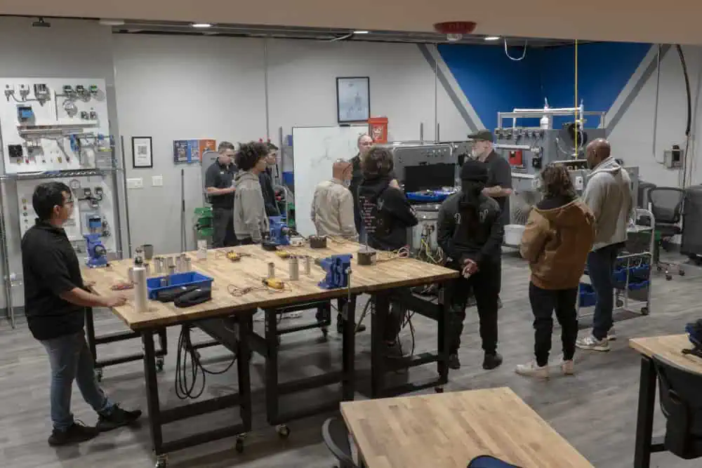 People are standing in a room with tables and chairs, participating in discussions and networking with one another Image