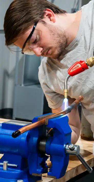 Person using a torch to heat a copper pipe secured in a vise