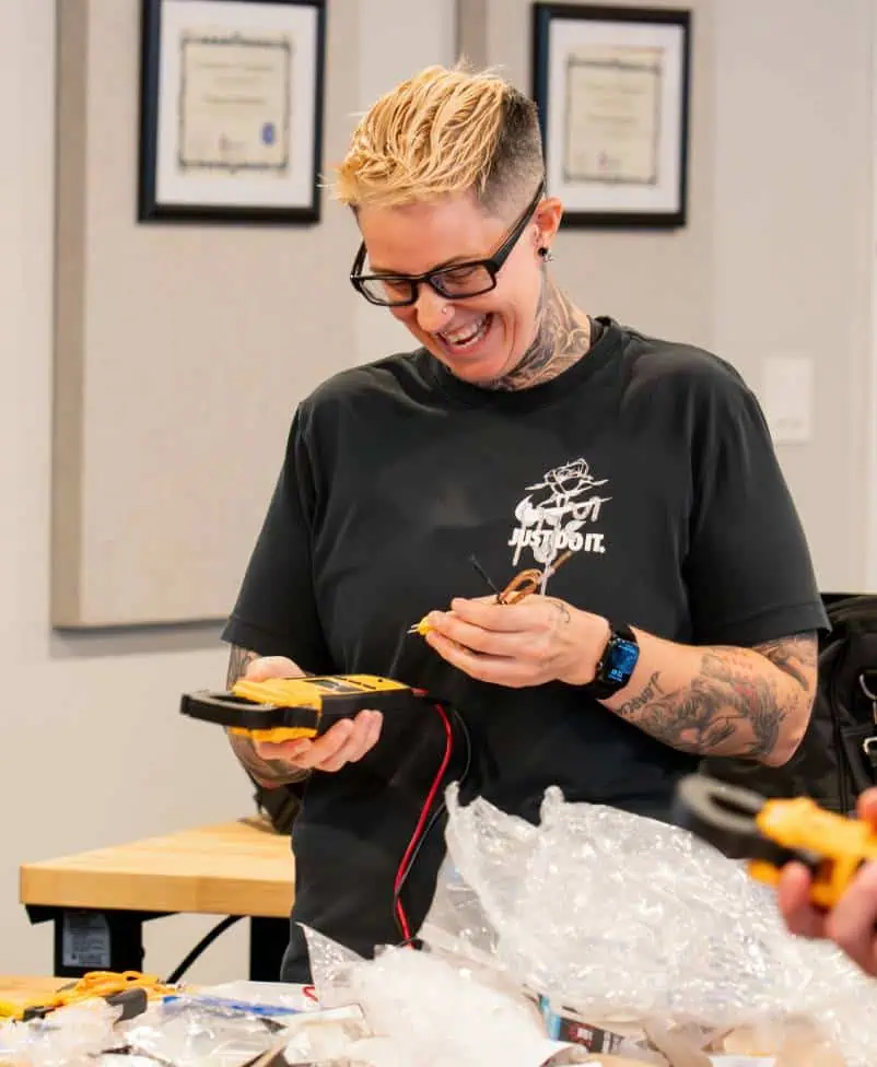 Smiling trainee using a multimeter at a workshop table with tools