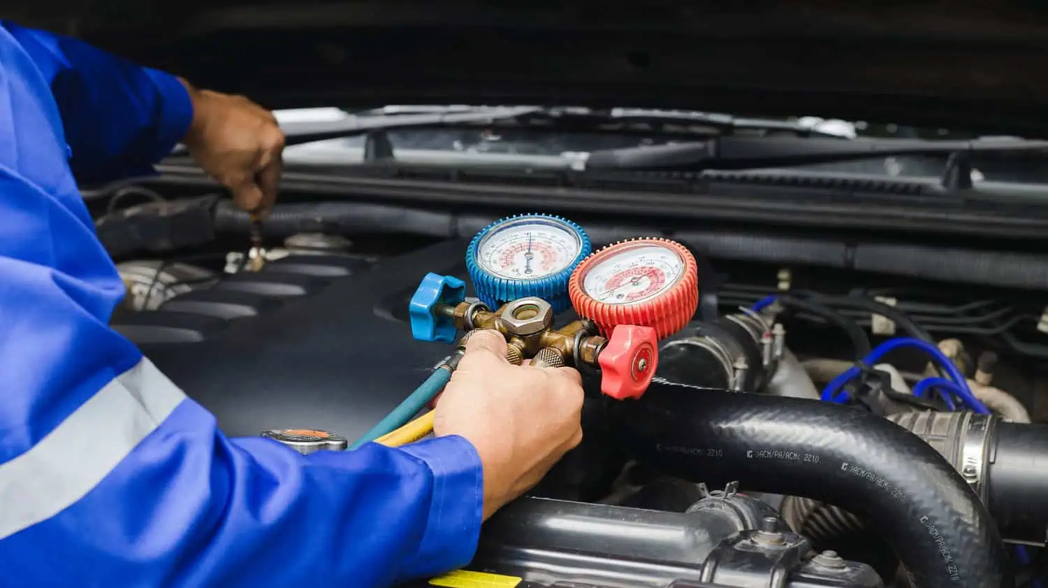 Technician checking a vehicle AC system with pressure gauges.