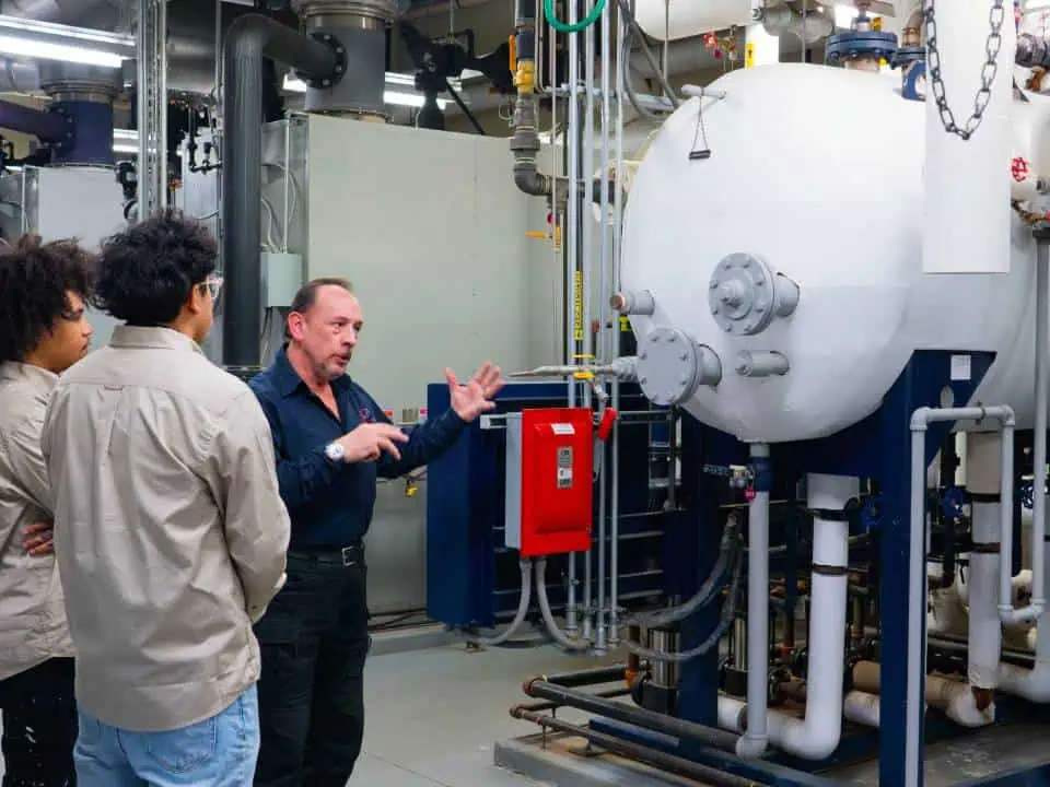 Three people inspecting an industrial boiler in a technical facility