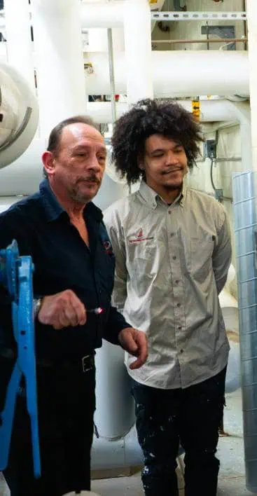 Two men standing together in an industrial setting, one holding a flashlight
