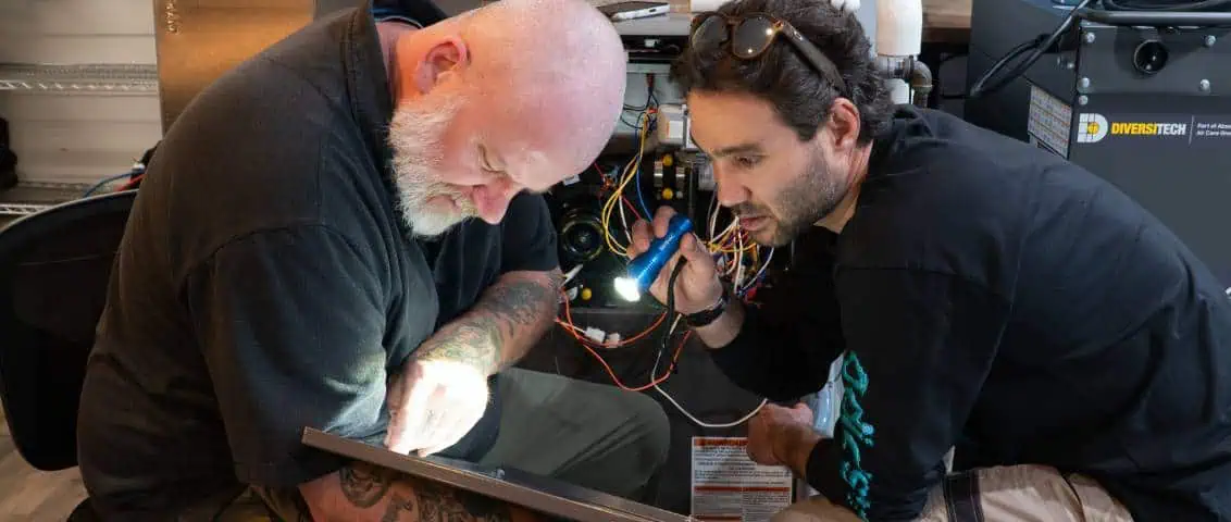 Two men working on electrical wiring inside a machine