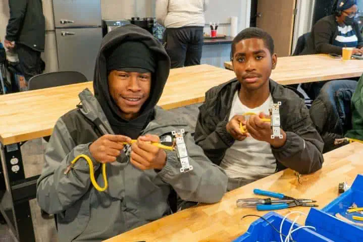 Two young men working on electrical wiring projects in a workshop